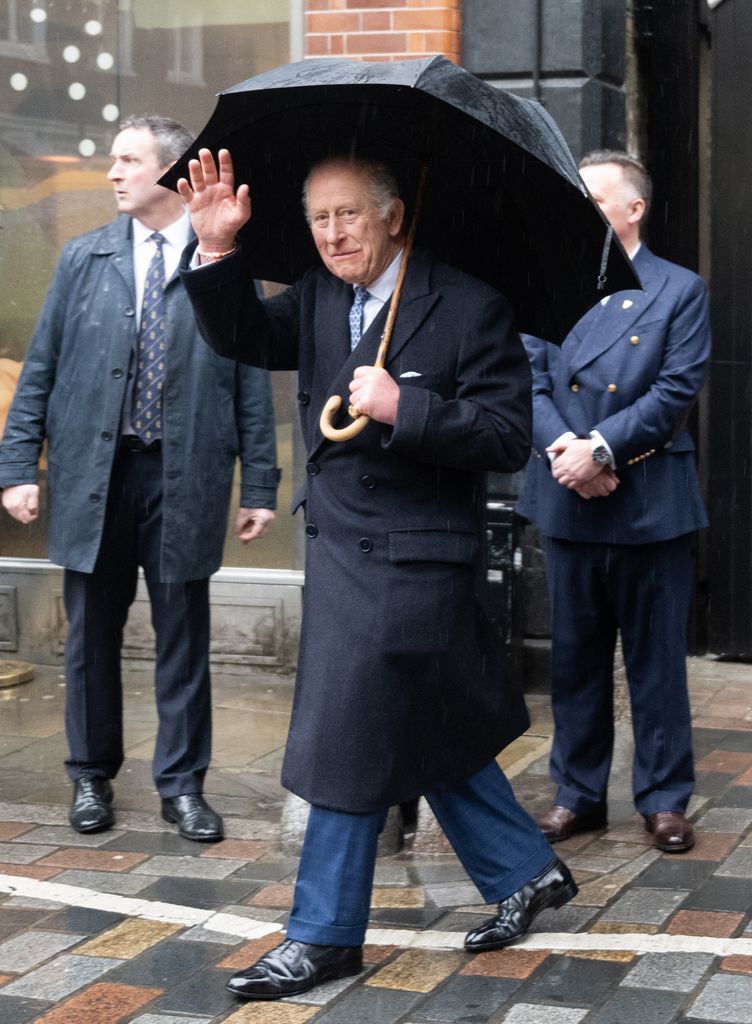 King Charles waving while under an umbrella