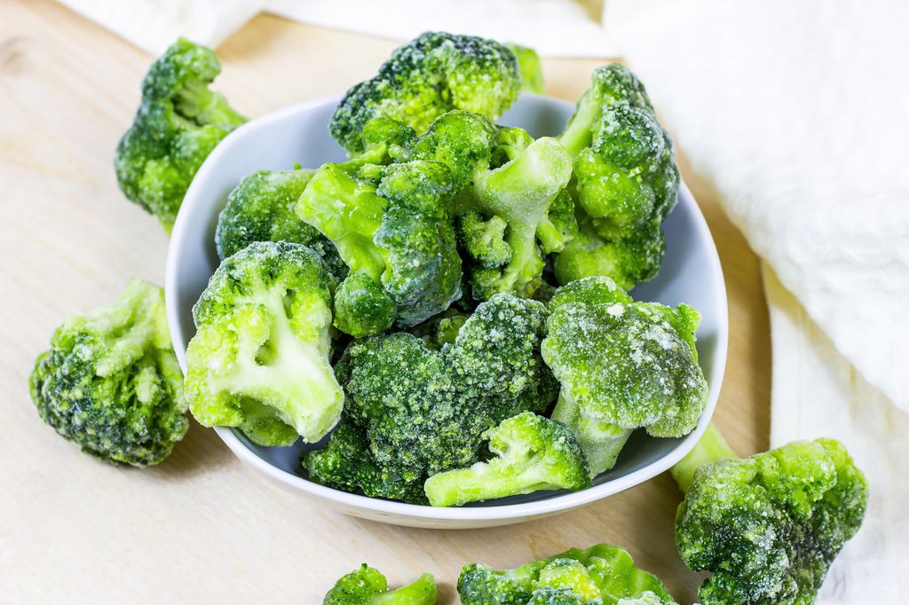 Fresh green frozen broccoli in small white bowl on light background.