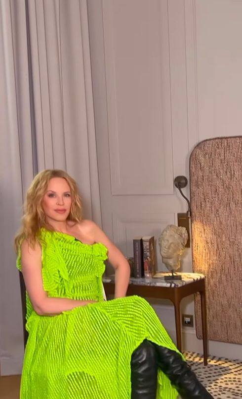 Kylie Minogue sitting in a neon-green dress and leather boots