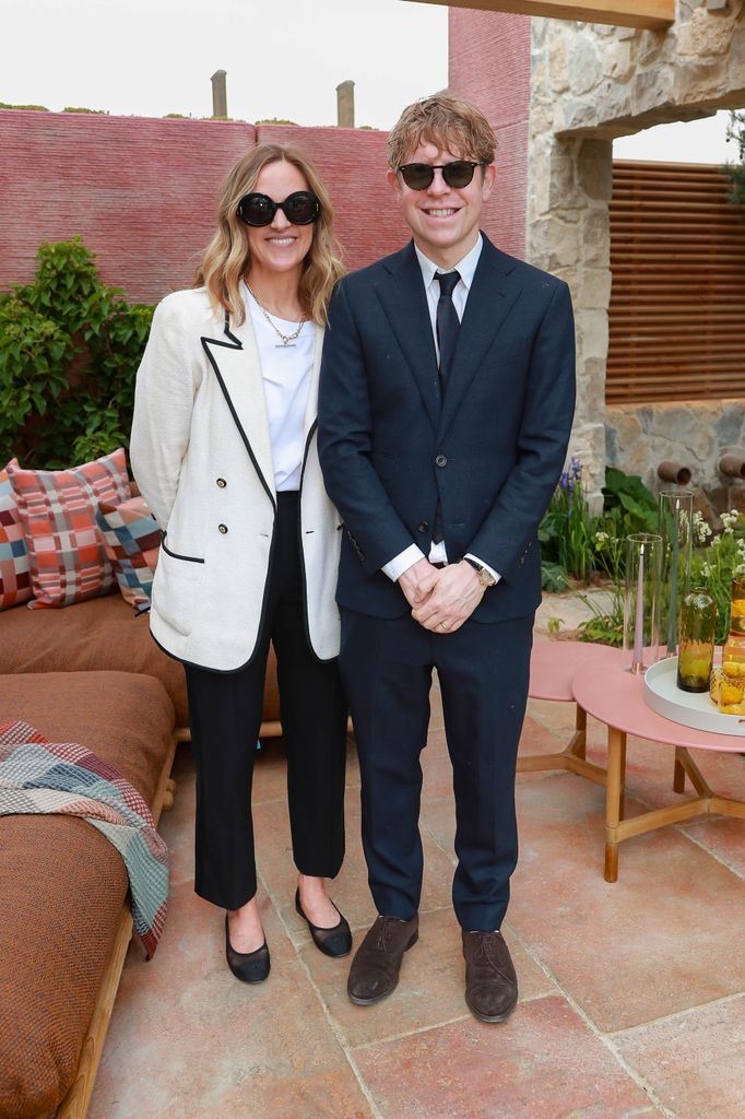 Rose Hanson in a cream jacket and black trousers stands beside Josh Widdicombe in a dark suit and tie at the chelsea flower show.