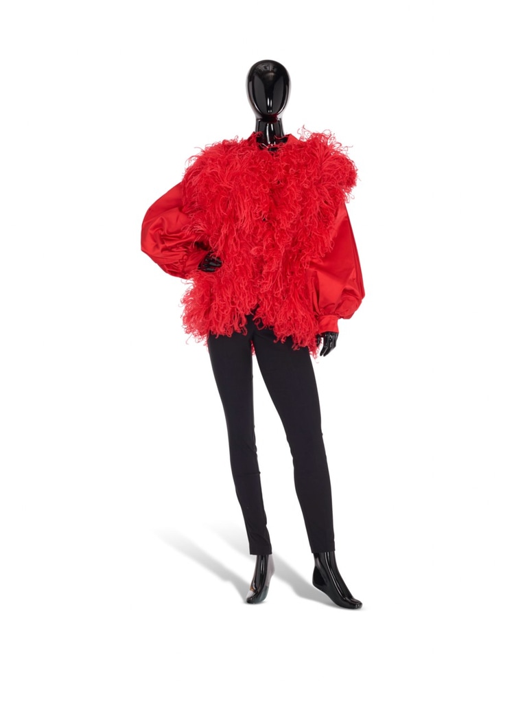 A vibrant red coat with voluminous, feathery details on the sleeves and body by Christian Dior Boutique (Circa 1990). The coat has a bold, dramatic silhouette, emphasizing its texture and movement. It is paired with simple black pants to balance the statement piece. This extravagant coat once belonged to Iris Apfel.