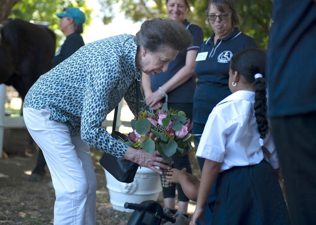 Princess Anne wearing white trousers bending down to look at flowers