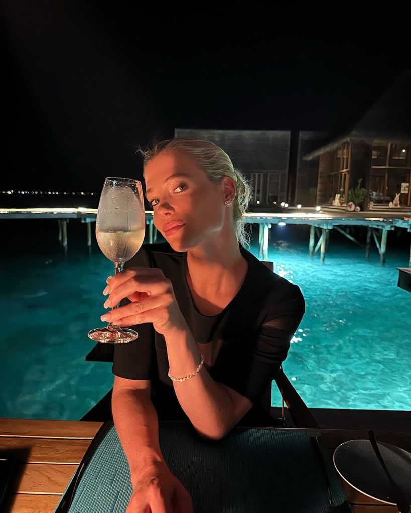 Lady Amelia holds a glass of wine as she rocks a black dress in the Maldives