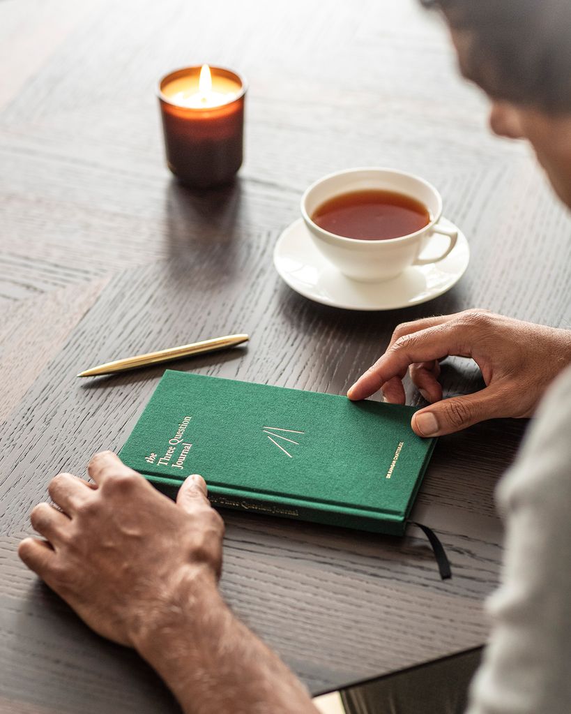 journal on a desk next to a candle and coffee