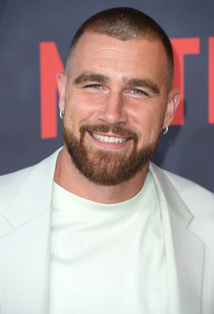 Travis Kelce smiling in a white suit jacket 