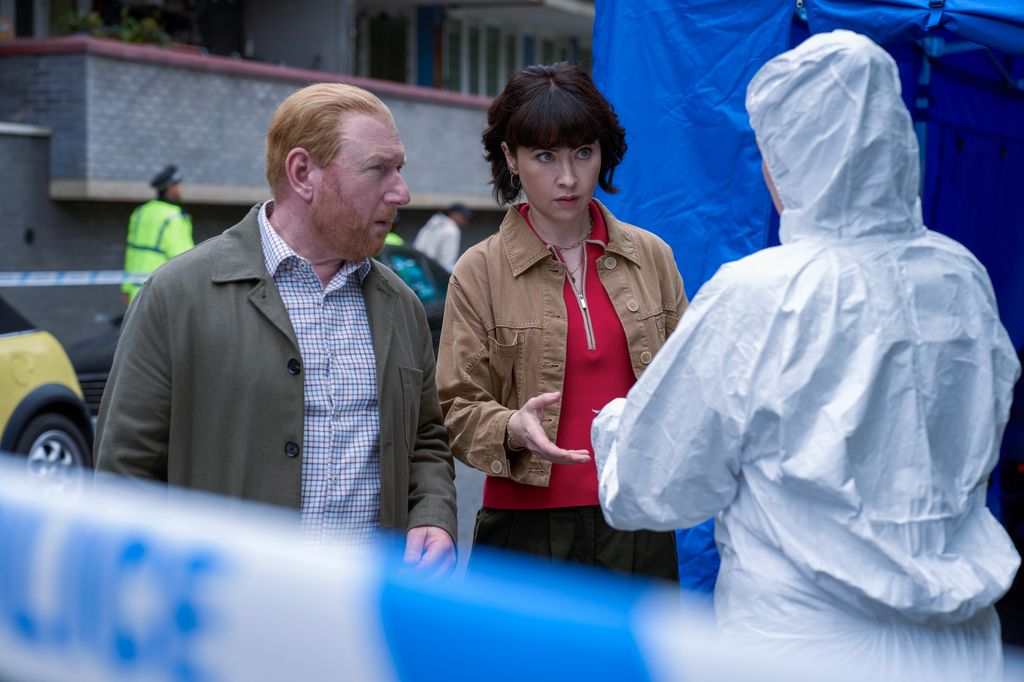 police officers standing next to woman in forensic suit in front of blue police tape
