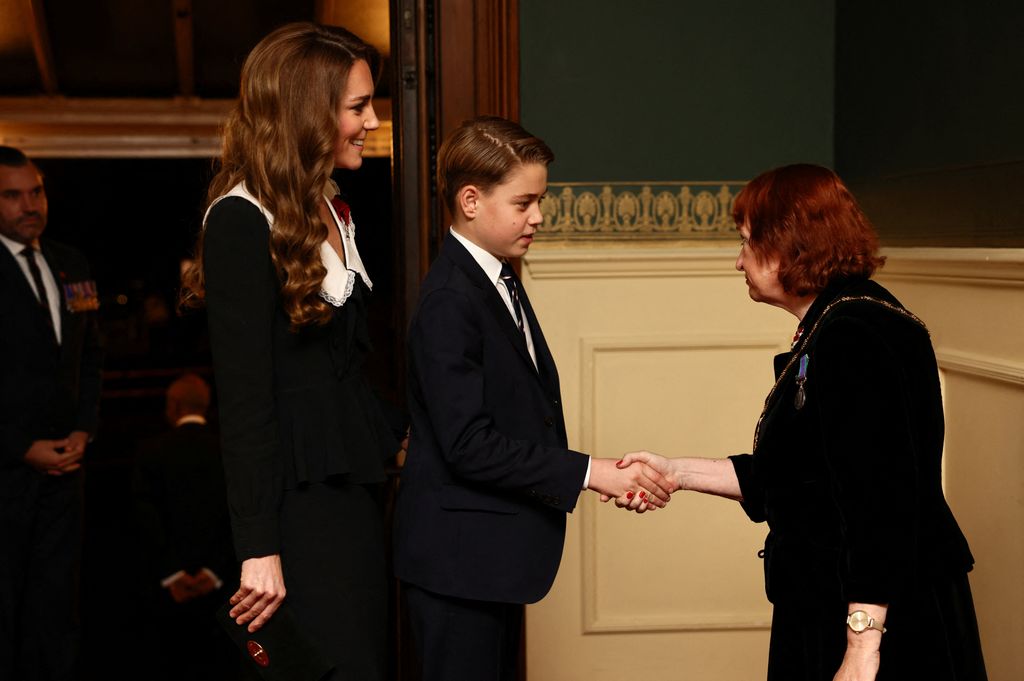 Prince George shaking hands with a woman with Kate Middleton smiling behind him