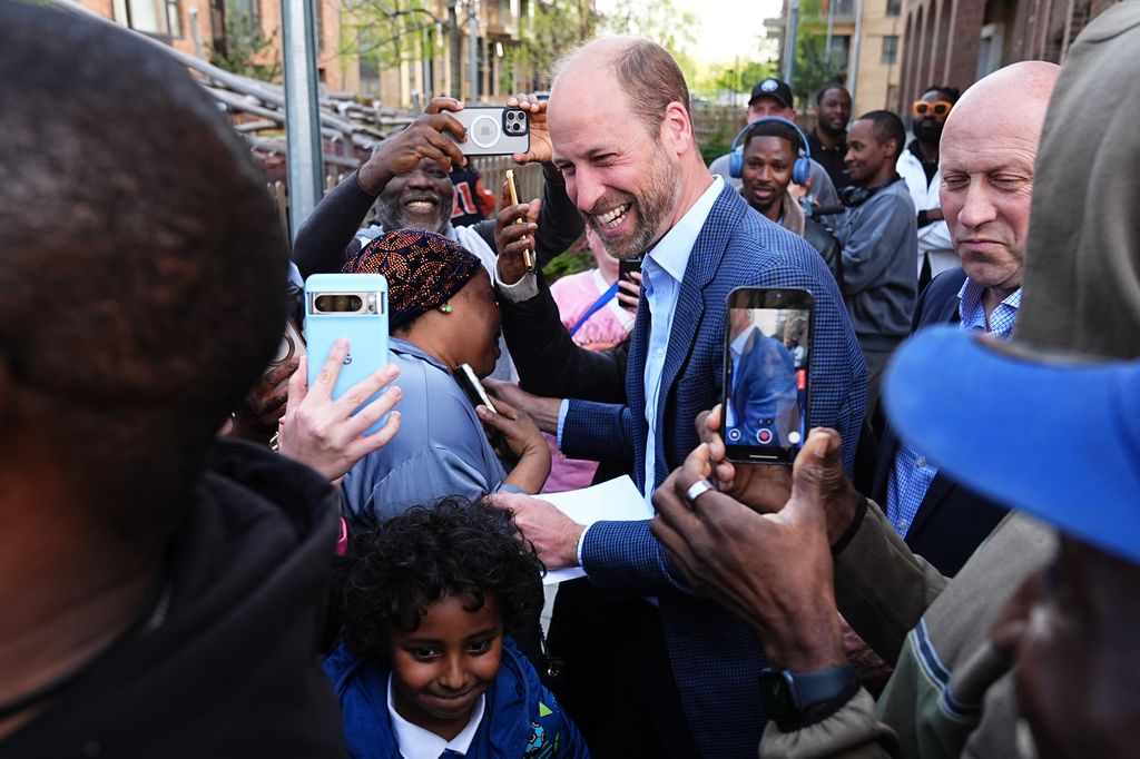 Prince William looking happy as he stops to take photos with a crowd of people outside the community centre 