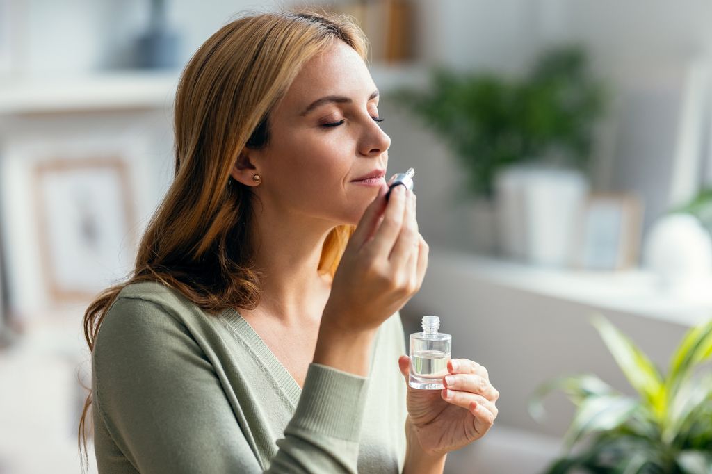 Shot of a beautiful woman holding a bottle of essential oil while testing it sitting on a couch at home.