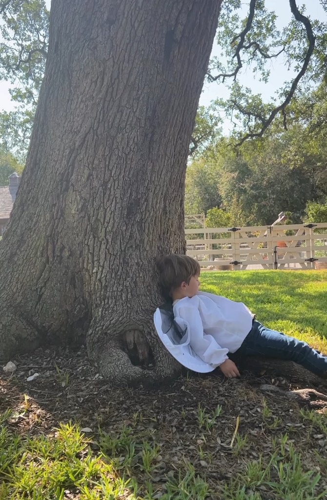 Still from a video shared by Joanna Gaines on Instagram August 2023 where her son Crew is resting against a tree after harvesting honey from their bee farm with his mom