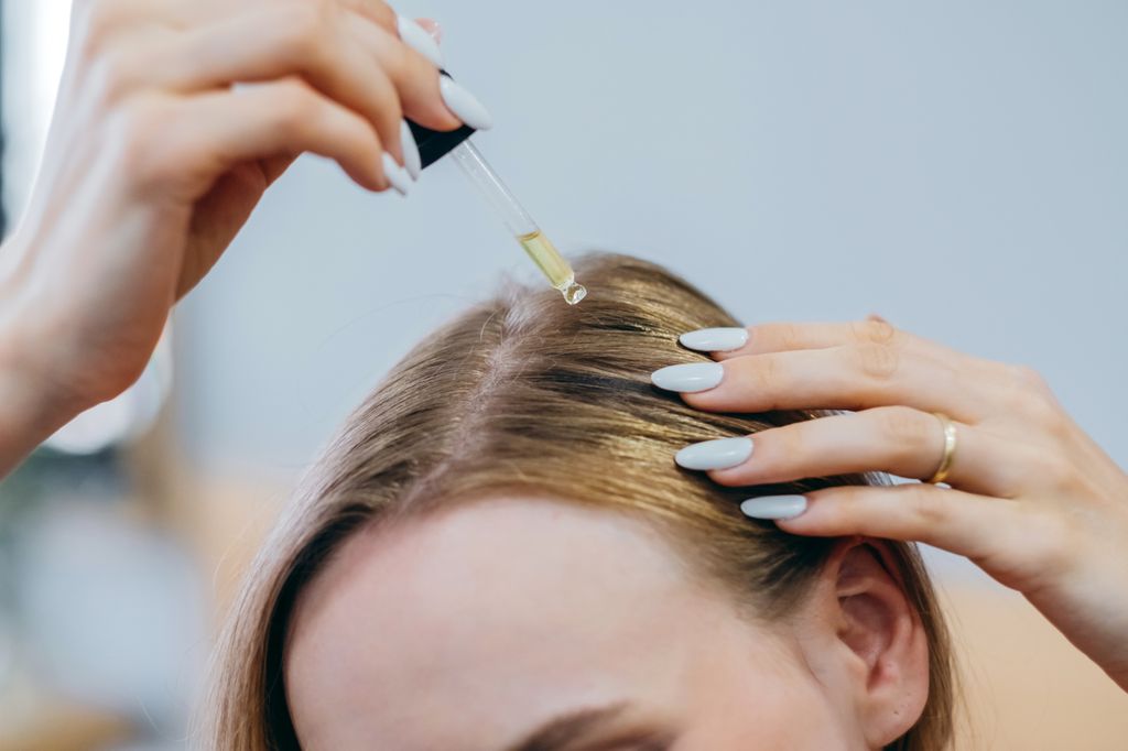 Close up woman applies oil to her hair with pipette. Beauty caring for scalp and hair