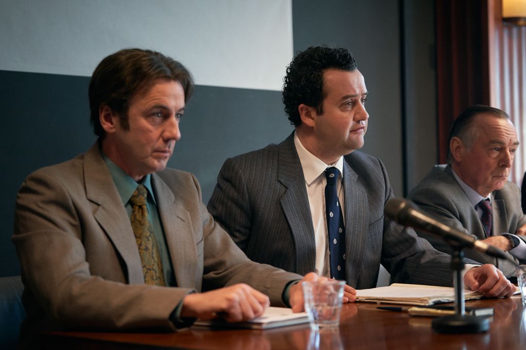 three men sitting on panel at press conference