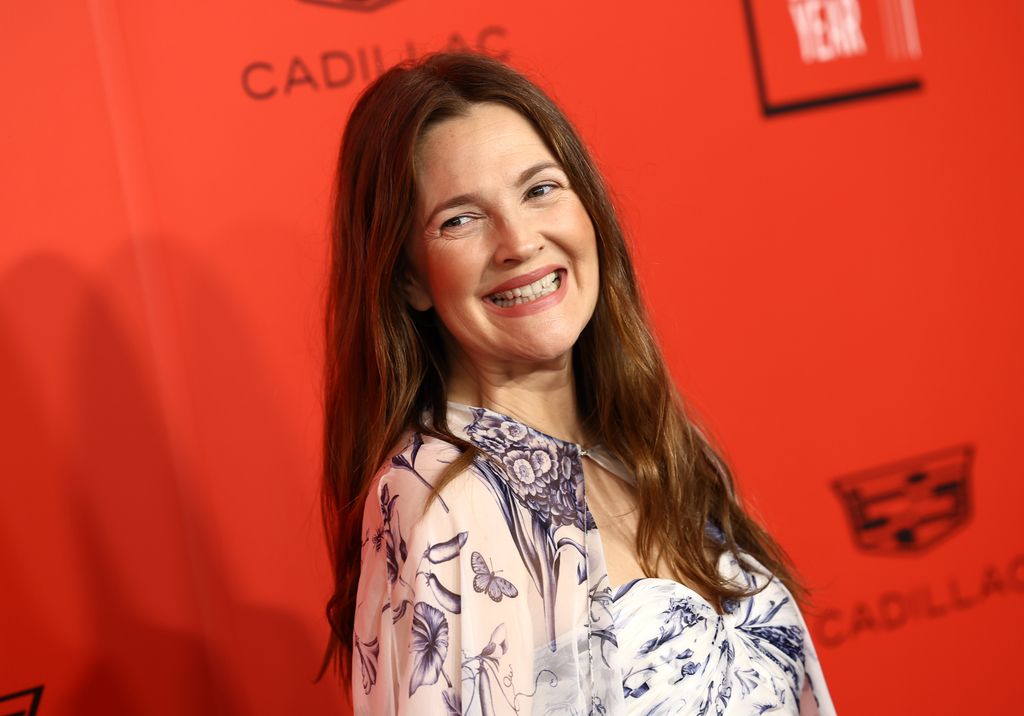 Drew Barrymore smiling in a printed dress on a red background