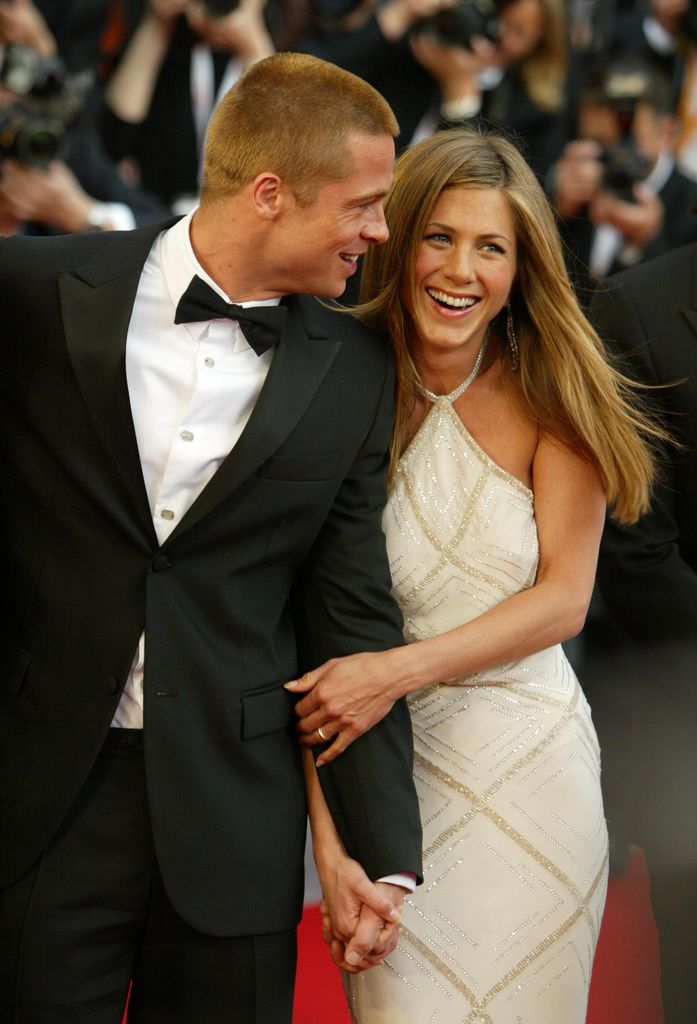 Jennifer Aniston in a white dress holding hands with Brad Pitt