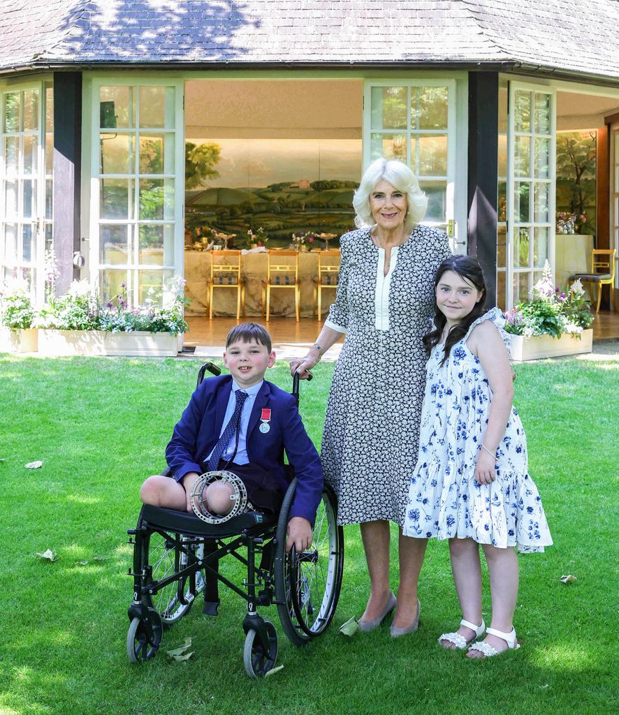 A young boy in a wheelchair alongisde Queen Camilla and a young girl in a floral dress