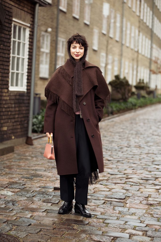 Katerina Chekan wears black pants, brown long coat with tassels, brown knitted hat and light peach pink bag outside the OpÃ©raSport show during the Copenhagen Fashion Week Autumn/Winter 2025 on January 27, 2025 in Copenhagen, Denmark