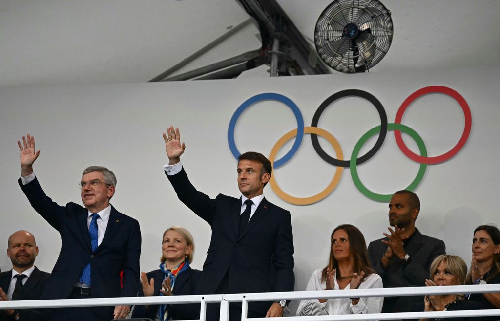 Emmanuel Macron and Thomas Bach waving in front of the Olympic Rings