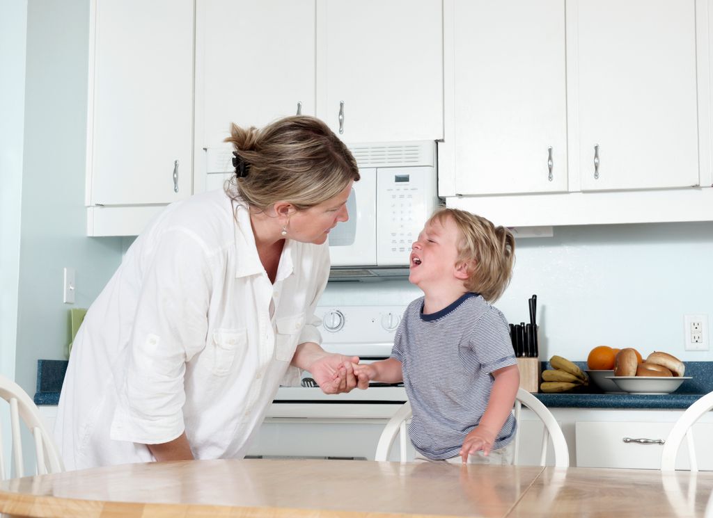A mother trying to calm her crying toddler at home in their kitchen.  