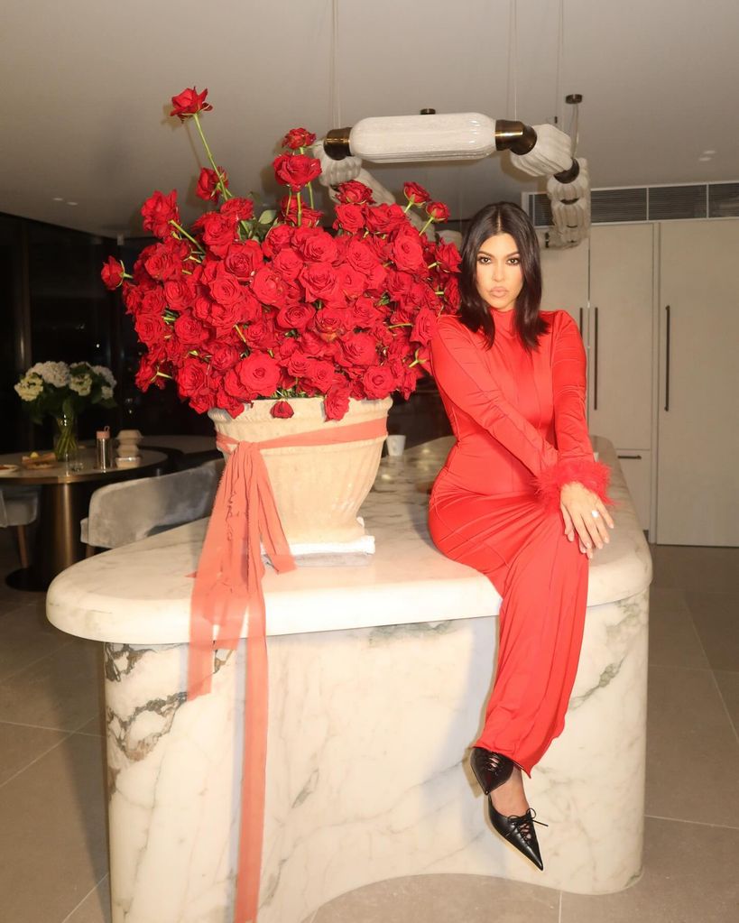 kourtney kardashian wearing red dress posing by bouquet of roses