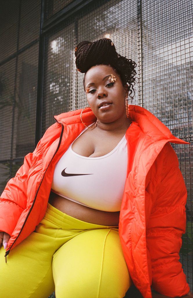 Black woman in orange jacket and white Nike crop top