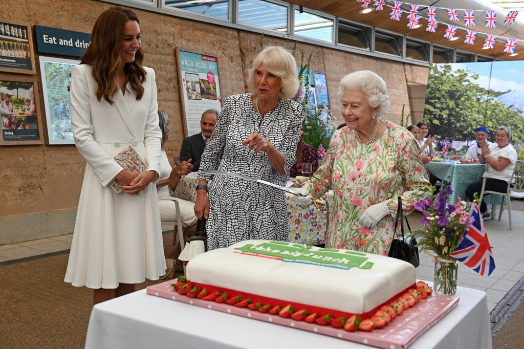 Queen Elizabeth II (C) considers cutting a cake with a sword, lent to her by The Lord-Lieutenant of Cornwall, Edward Bolitho with Princess Kate laughing next to her