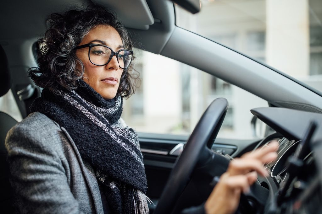 Mature businesswoman driving a car searching location on her smartphone. Woman behind steering wheel using phone for navigation.