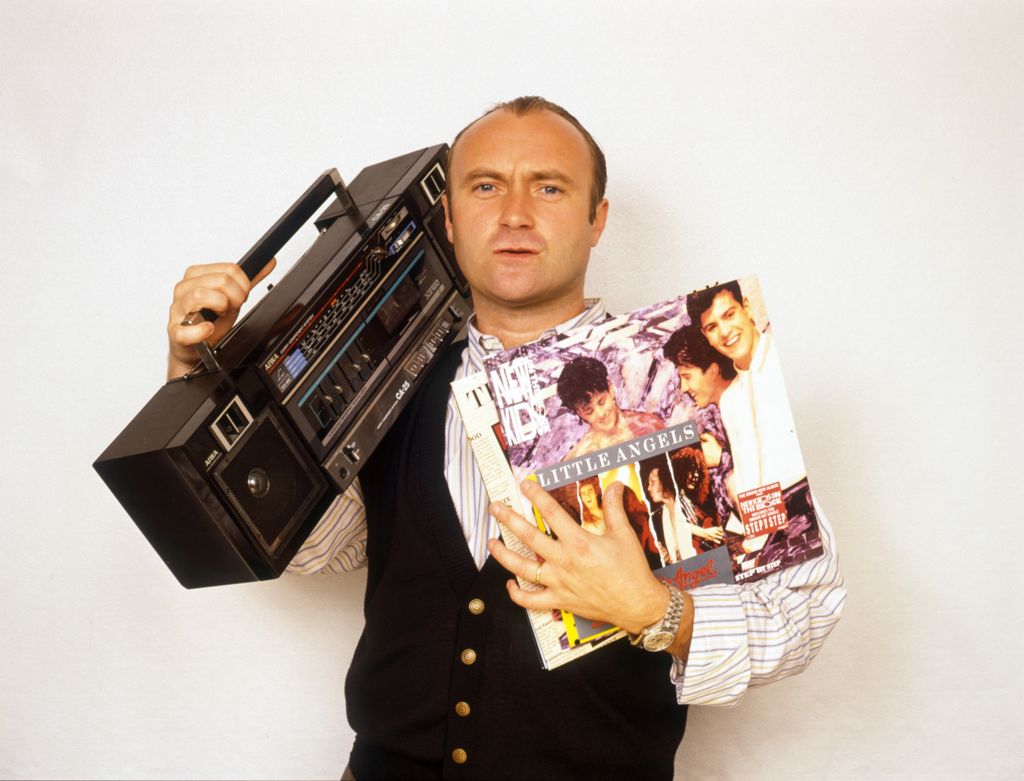 English drummer, singer-songwriter, record producer and actor Phil Collins of rock band Genesis, holding a portable radio and some records during a photo shoot, circa 1995.