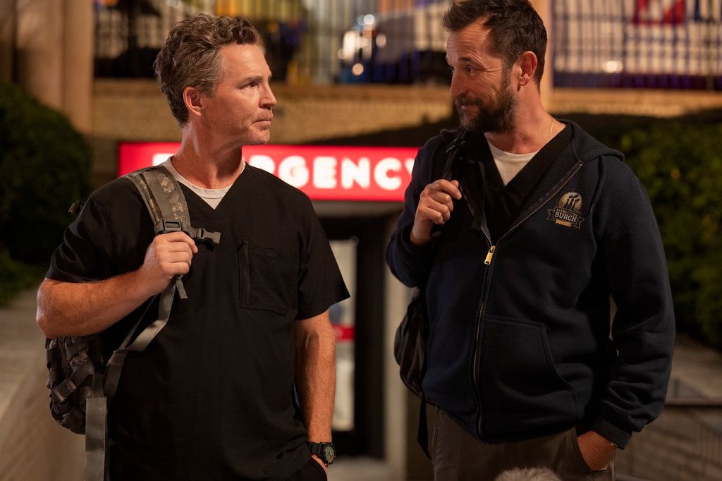 Robby and Abbott (played by Shawn Hatosy and Noah Wyle) exit the hospital and walk to the park in The Pitt