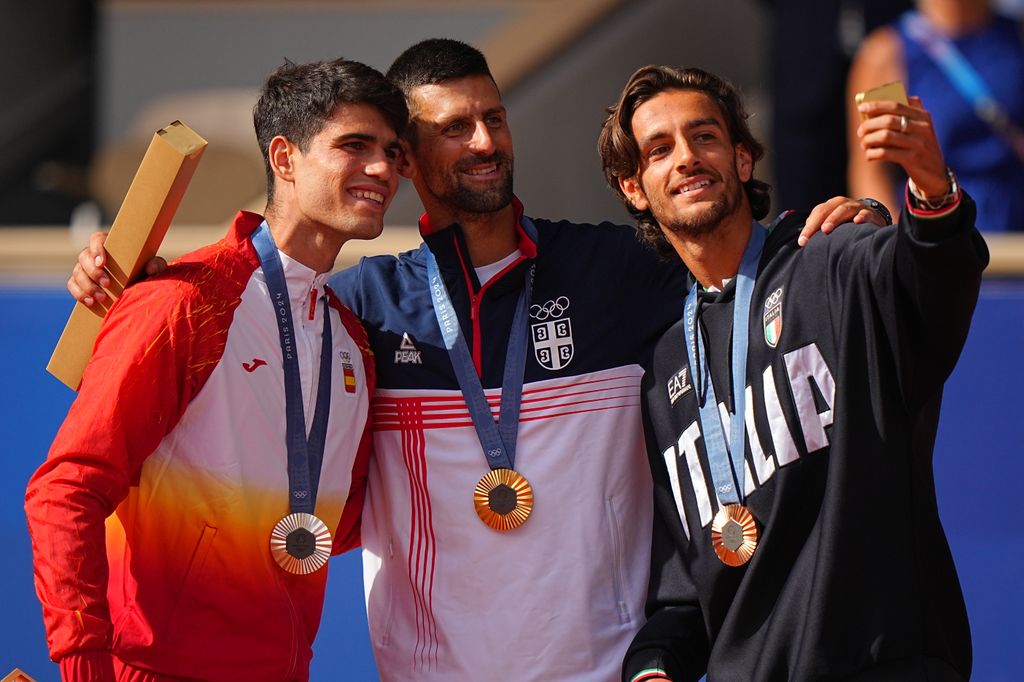 Team Spain and Silver medalist Carlos Alcaraz, Team Serbia and Gold medalist Novak Djokovic and Team Italy and Bronze medalist Lorenzo Musetti pose for a selfie on the podium following the men's singles tennis event at Roland Garros