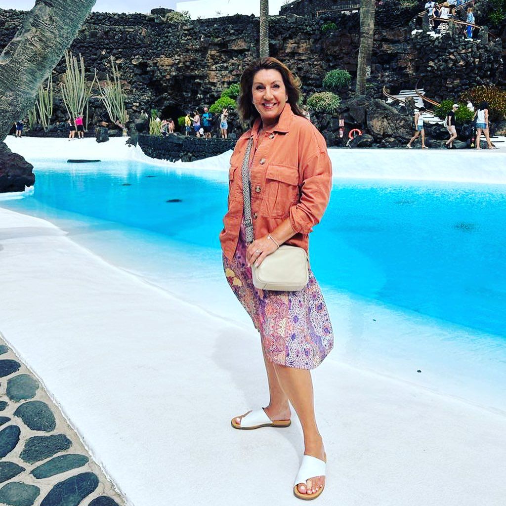 Jane McDonald beaming as she stands by the side of a pool 