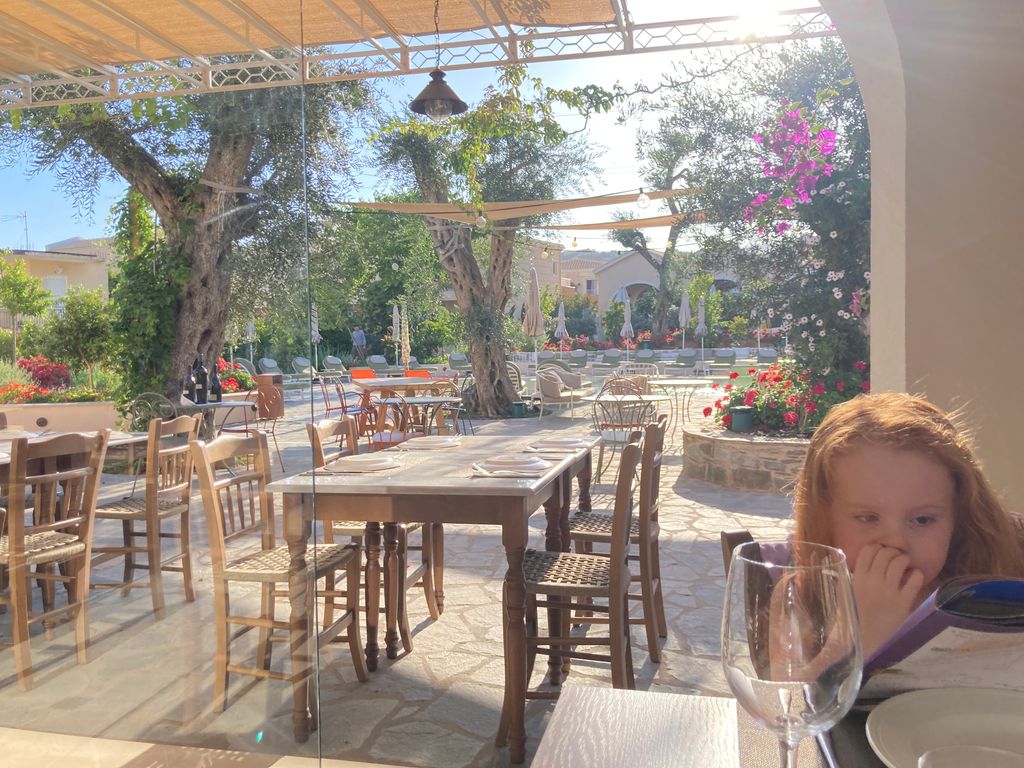 Little girl at restaurant table with empty chairs and tables and trees in the background