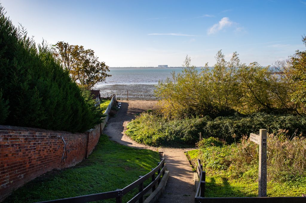Monkey Steps on Mersea Island with sea in the distance and bushes and and wall partially bathed in sunlight