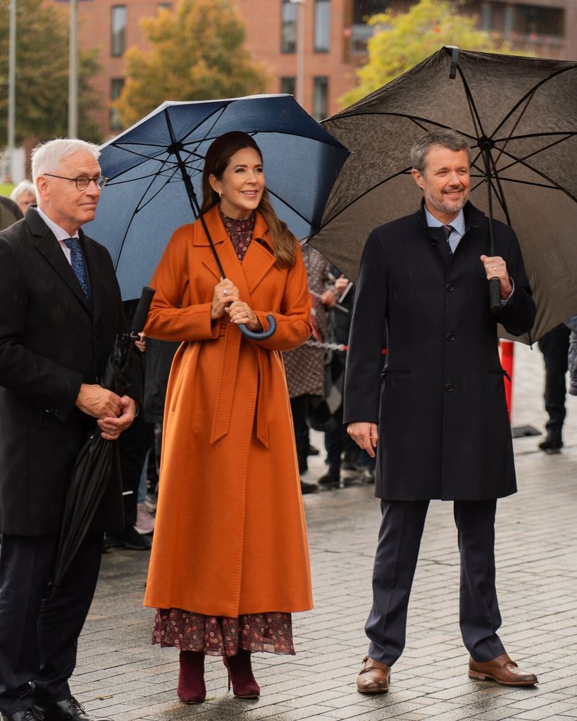 Queen Mary in orange coat under umbrella with frederik