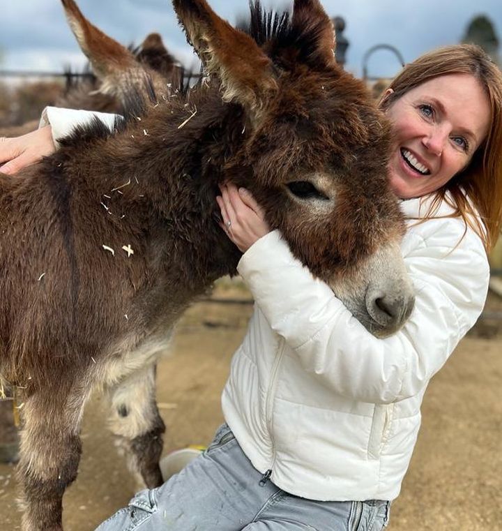 Geri Horner wearing white coat hugging a donkey