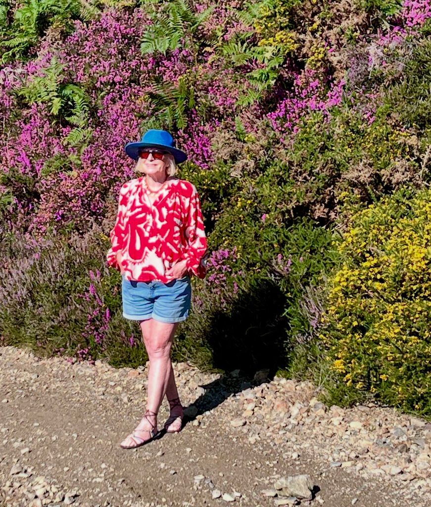 Woman in a blue hat standing in front of a flowering bush