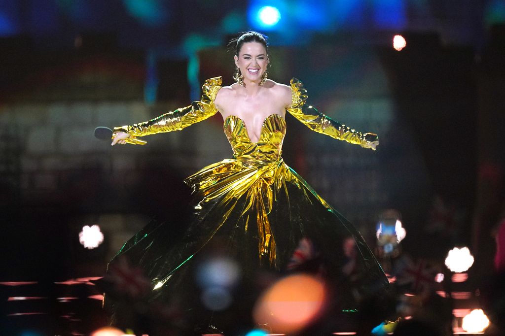 Katy Perry smiling on stage in a gold dress