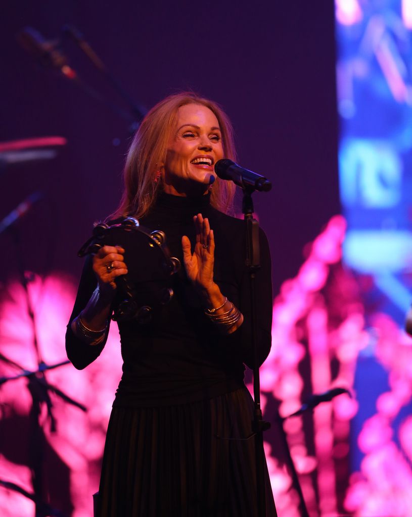 Belinda Carlisle tient un tambourin et se tient devant un microphone sur scène.