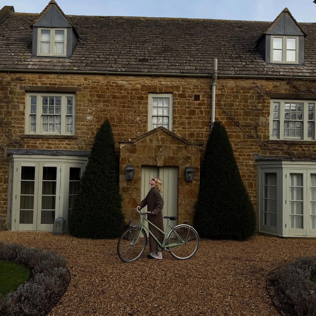 Sydney Sweeney stands outside a cosy brick building with a mint green bicycle