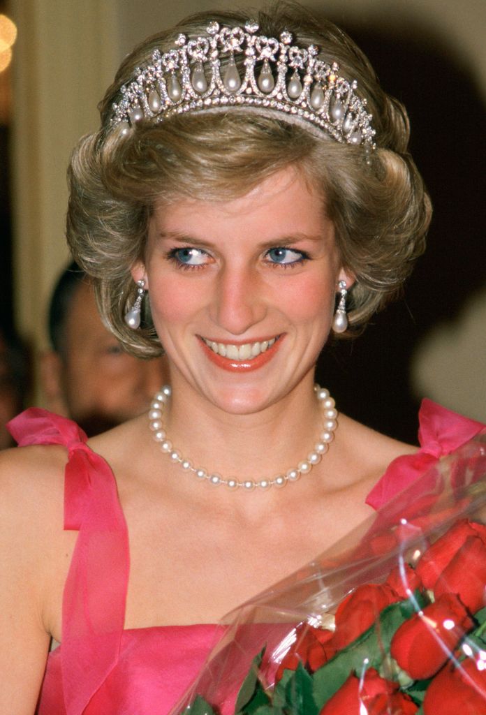 The late Princess Of Wales in a pink dress and tiara holding a bunch of roses