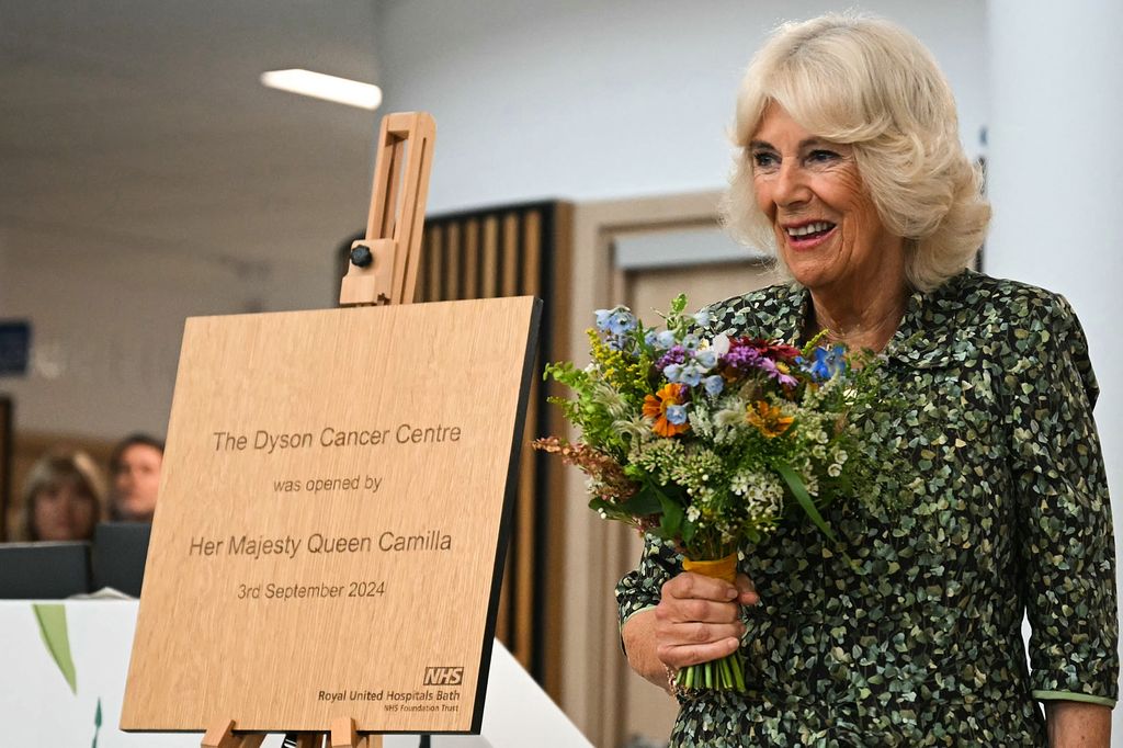 camilla holding bouquet of flowers next to wooden plaque