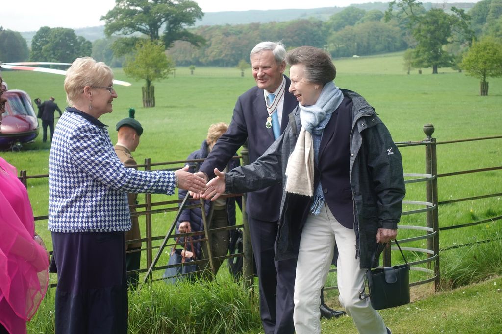 Princess Anne wearing two scarves and shaking hands with a woman