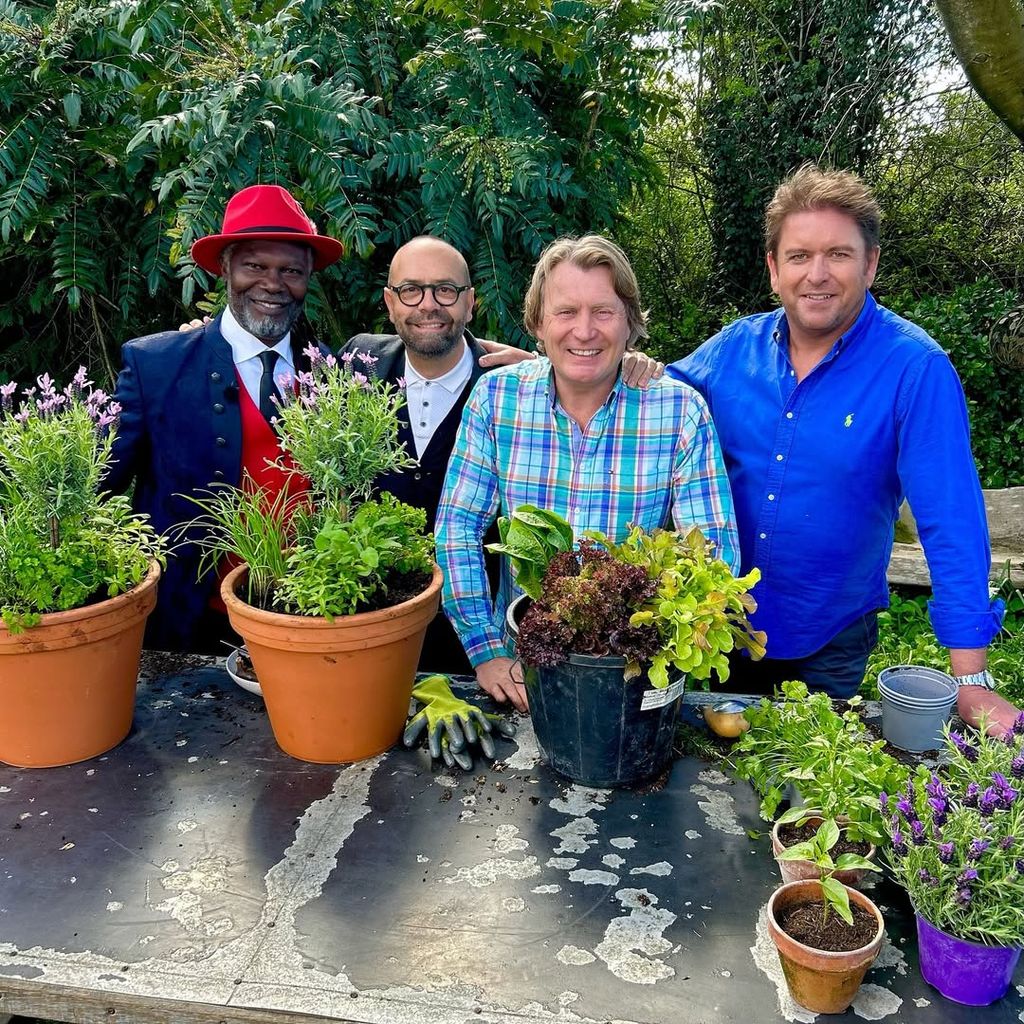 James Martin stands with three guests in his garden filming Saturday Kitchen in front of large table covered in pots