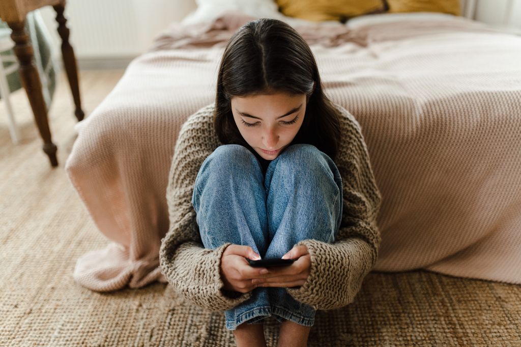 Teenage girl sitting on the floor and scrolling her smartphone.