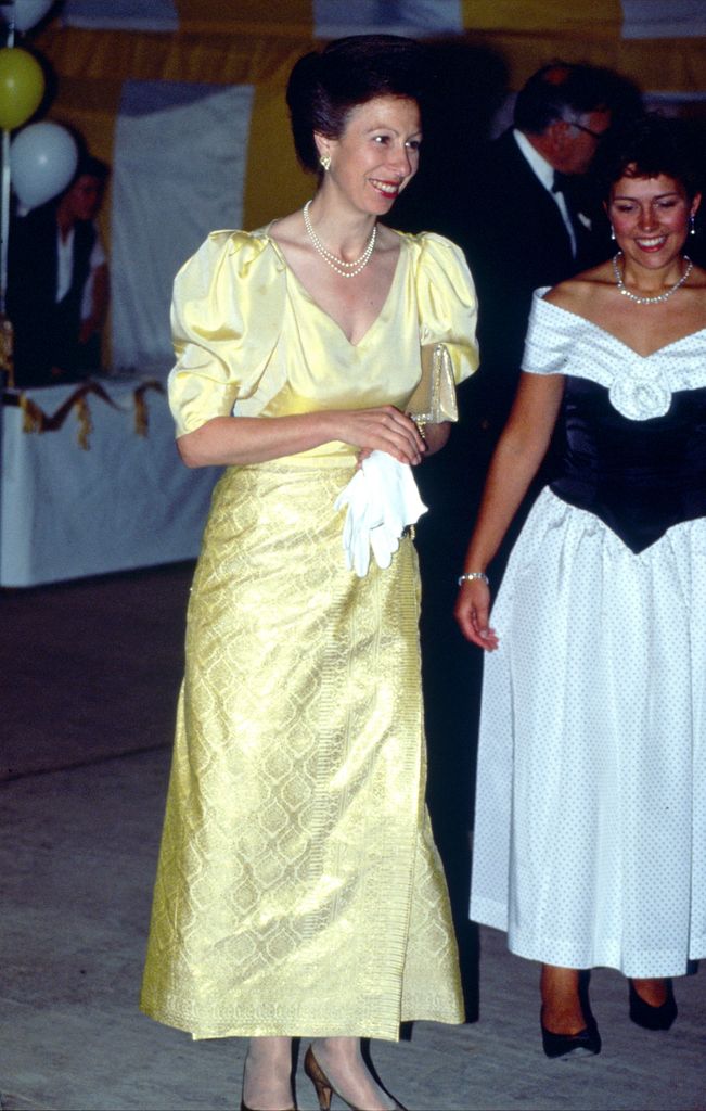 La princesse Anne portant une longue robe jaune en soie sourit 
