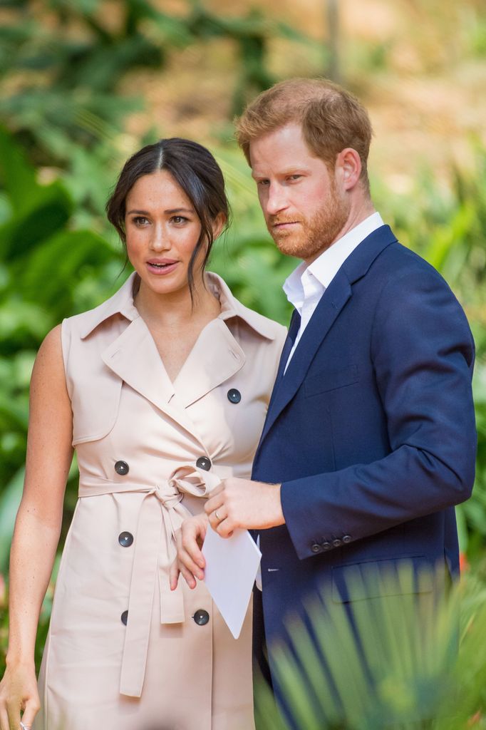 Prince Harry in a blue suit with Meghan Markle in a sleeveless dress