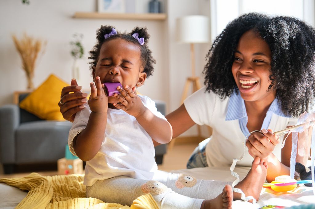 woman playing with a child who is putting a purple block in her mouth