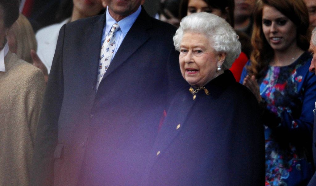 The late Queen Elizabeth II standing and wearing a cloak