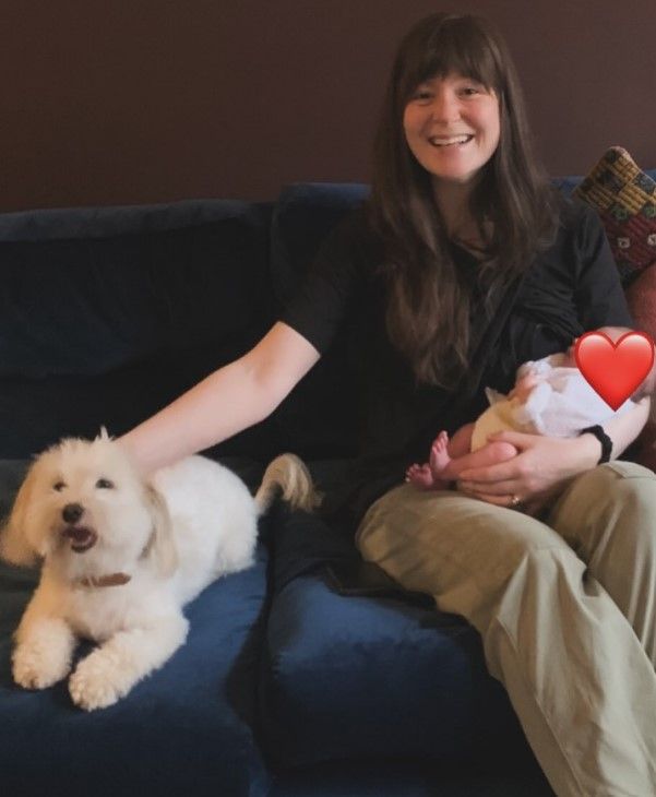 Natasha smiles as she holds baby Jean and strokes her dog 