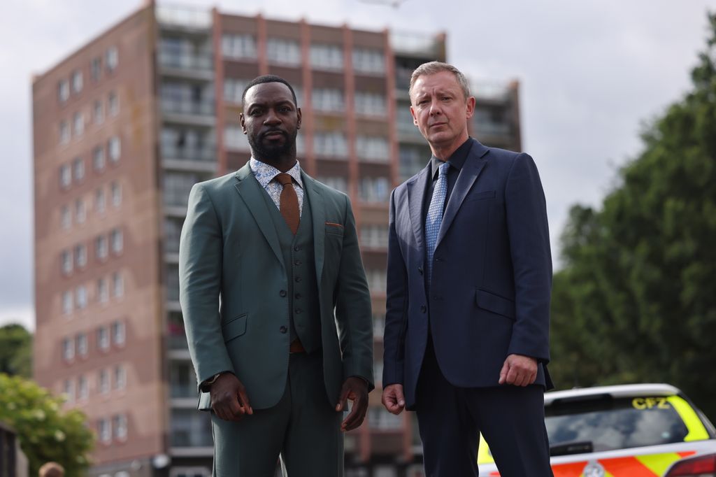 Two men in suits that stand in front of a police car