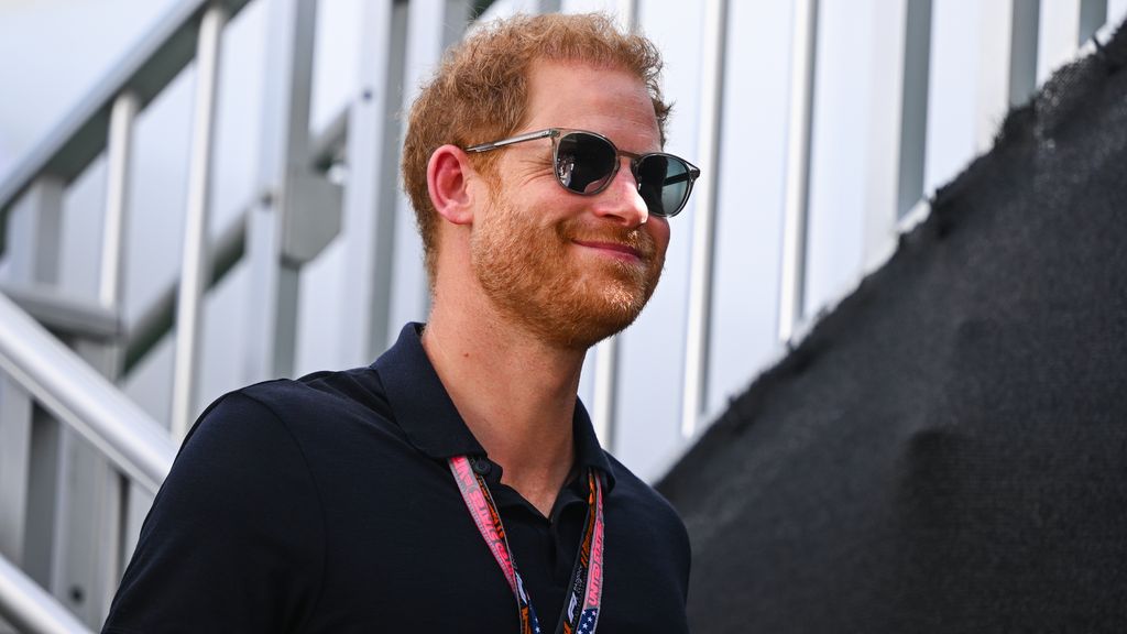 Prince Harry smiling and walking while wearing sunglasses